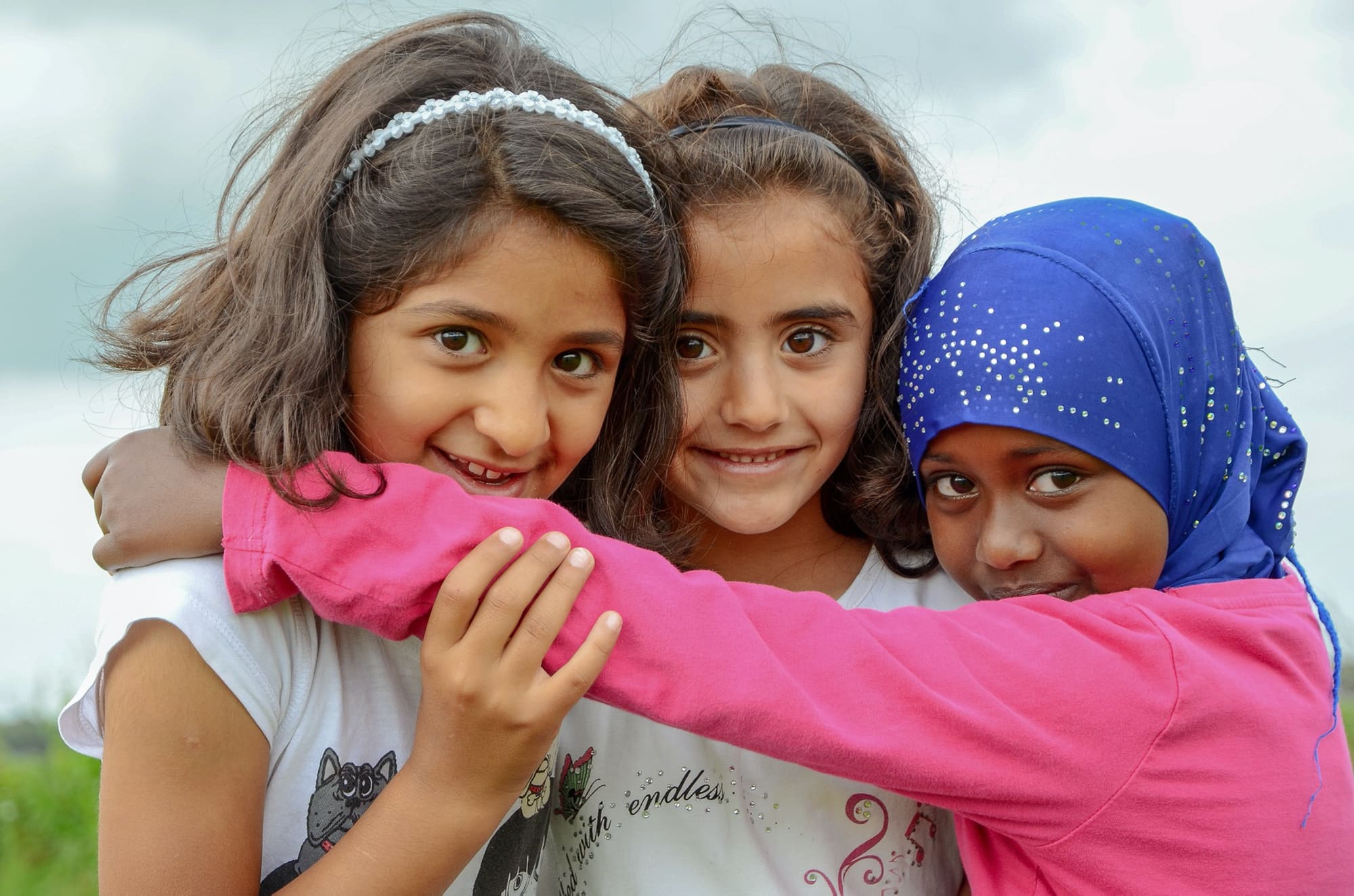 3 junge Mädchen mit verschiedenem Migrationshintergrund und Kopftuch umarmen sich lachend